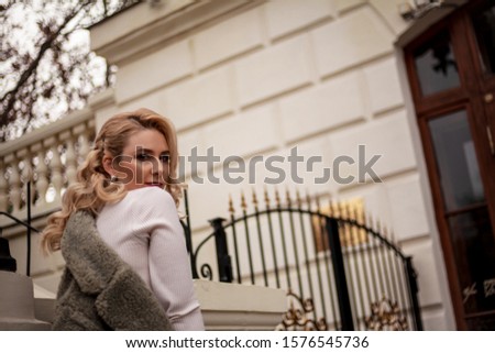 Fashion woman walking at the street, dressed modern clothes. Female moder wearing faux fur coat, tutleneck, skirt,