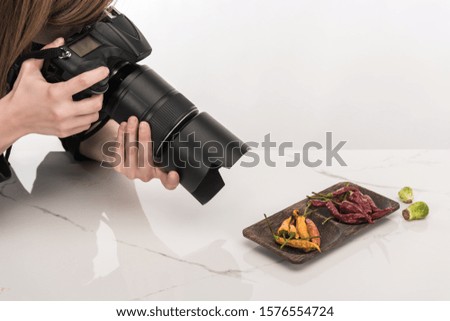 cropped view of female photographer making food composition for commercial photography and taking photo on digital camera on white