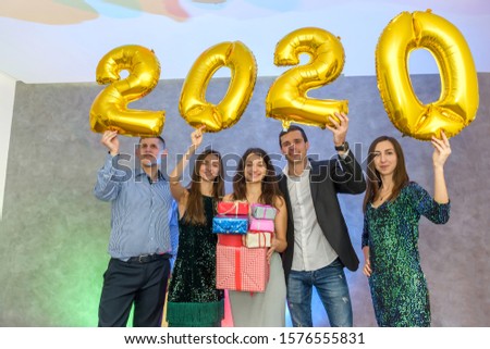 Cheerful company of friends with golden air balloons and present box celebrating New Year