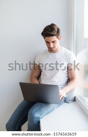 The courageous, handsome, a student working on a windowsill with a laptop. worker communicating on the Internet. Funny man play for laptop