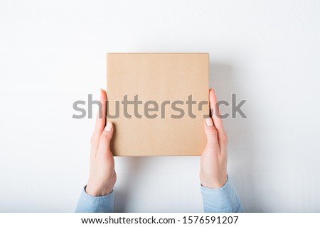 Square cardboard box in female hands. Top view, white background Royalty-Free Stock Photo #1576591207