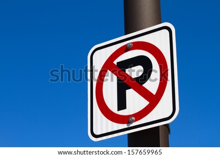 Sign showing a capital P with a red circle denoting a no parking area is attached to a pole against a blue sky.
