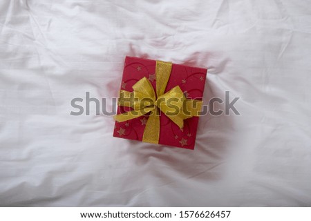 Christmas morning with gift box on white blanket on bed. Xmas present with red ribbon. Happy new year and winter holidays
