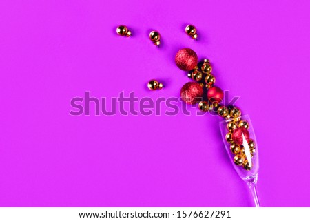 Golden and red christmas balls in a wine glass. Purple background. Flat lay, top view, copy space.