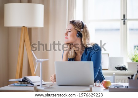 Young woman engineer with headphones sitting at the desk indoors in home office. Royalty-Free Stock Photo #1576629223