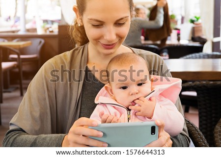 Mother and baby outddors in a restaurant watching carttons, making selfie