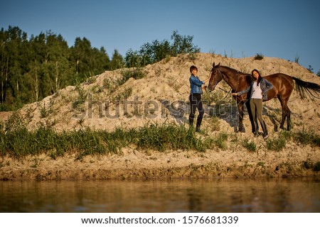 Two young women are walking with a horse on the lake. sunset sun