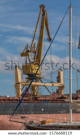 Industrial Crane. Big yellow crane with sailboat in the front of photo and sky with clouds in the background. Stock image.