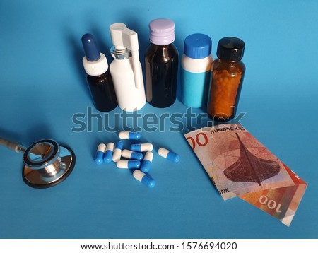 Norwegian banknote of 100 kroner, stethoscope, medicine bottles and pills on the blue background