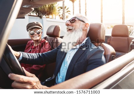 Happy senior couple having fun on new convertible car - Mature people enjoying time together during road trip vacation - Elderly lifestyle and travel transportation concept Royalty-Free Stock Photo #1576711003