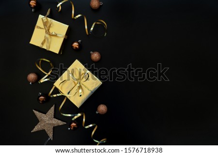 Gift boxes wrapped golden paper and ribbon decorated streamers and baubles on black background. Top view. Flat lay.  Christmas and New Year holidays concept. Copy space