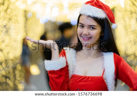 Portrait of a cheerful Asian woman wears Santa Claus costume in Christmas festival with beautiful bokeh light background.