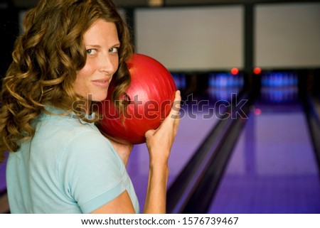 Woman in a bowling alley, holding a red bowling ball