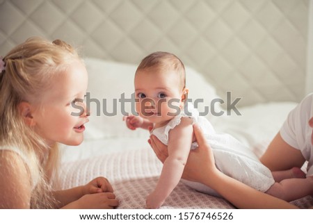 Young beautiful mother holds a baby. Little sister kisses her little sister. Baby. Children bedroom. Cozy.