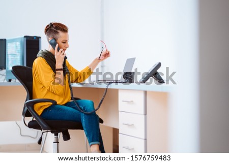 Businesswoman sitting at the desk and using landline phone in the office Royalty-Free Stock Photo #1576759483