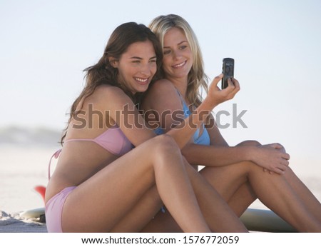 Two young women in bikinis taking a picture with their mobile phone