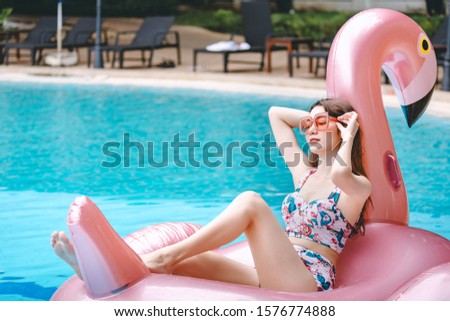 Happy bikini asian woman relax on big pink flamingo pool float in swimming pool at day, summer vacation concept, banner size