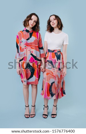 Two twin sisters holding hands full length picture. Standing in a blue studio