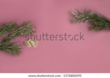 A Christmas toy - a wooden homemade in the form of a heart hanging on a pine branch with hoarfrost. On the right there is a free branch to insert your decorative toy. Flat lay on ash pink background.
