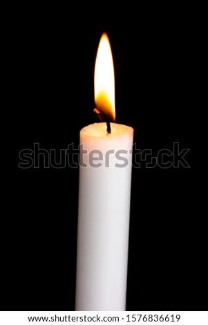 One isolated white candle burning on a black background. White candle flame in the dark