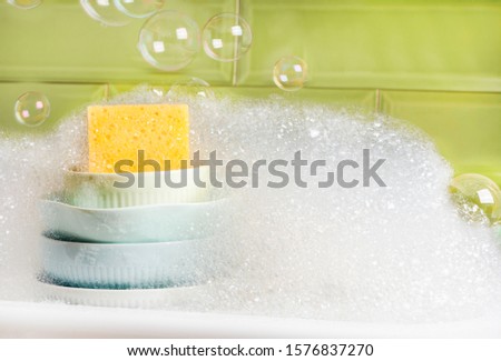 Washing dishes. Plates and foam in the kitchen sink, green ceramic tile background. Washing dishes in the kitchen, spring cleaning concept. Royalty-Free Stock Photo #1576837270