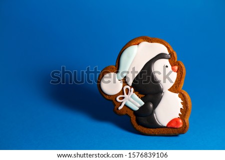 gingerbread cookie of cute penguin with gift on blue background. Traditional Christmas food. Christmas and New Year holiday concept