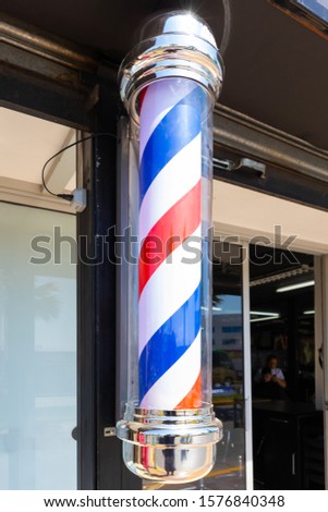 rotating barber pole with red white blue stripes hair salon shop sign in the morning