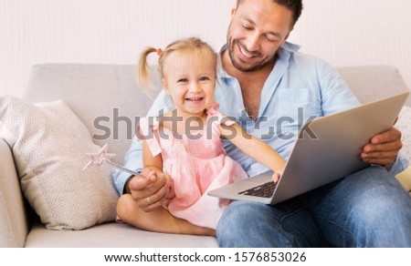 Family Weekend Concept. Little girl with wand sitting with father on couch using laptop. Empty space
