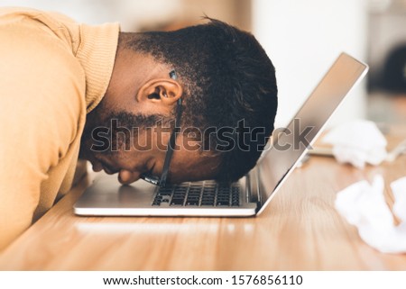 Desperate Employee. Depressed afro manager in eyewear resting head down on laptop keyboard