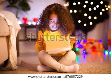 Xmas magic. Surprised little african american girl opening glowing Christmas gift, empty space