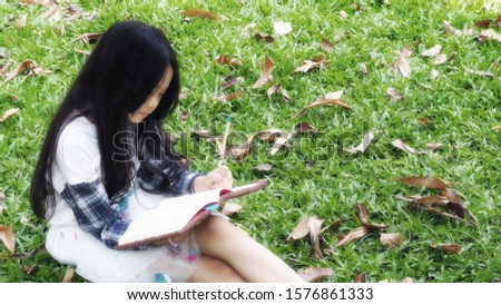 An Asian girl writing a book on the afternoon lawn