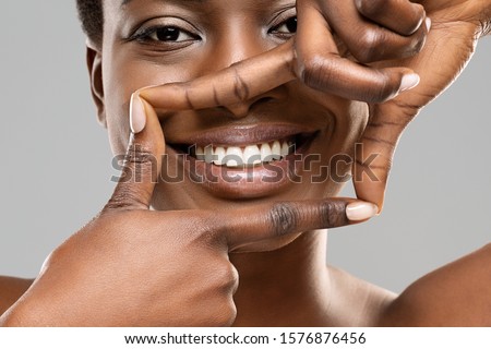 Frame your smile. Beautiful african woman framing her perfect white teeth with fingers, closeup Royalty-Free Stock Photo #1576876456