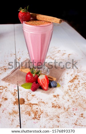 Photograph of a strawberry milkshake, with ground cinnamon and a piece of cinnamon and strawberries to decorate.