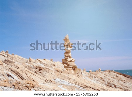 Landscape picture, pyramid of stones with the blue sea and sky background, sun light. Abstract.