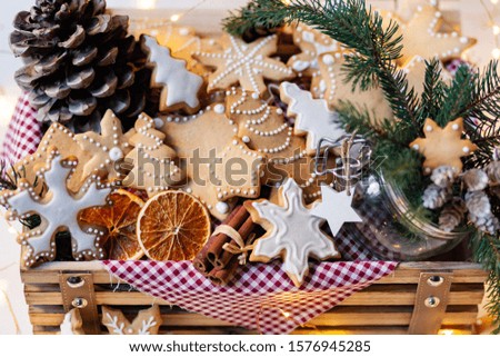 Wooden box with delicious homemade gingerbread cookies with white icing. Perfect beautiful gift in rustic style. Orange, cones, fir tree branches and lights as decor. Close up