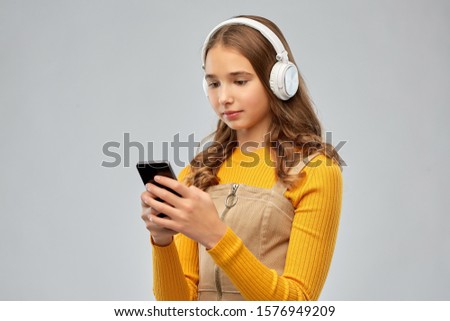 audio equipment and technology people concept - teenage girl in headphones listening to music on smartphone over grey background