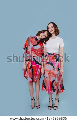Two twin sisters holding hands full length picture. Standing in a blue studio