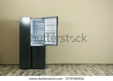 Modern refrigerator near beige wall, space for text