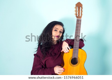 Beautiful young woman with brown guitar in studio