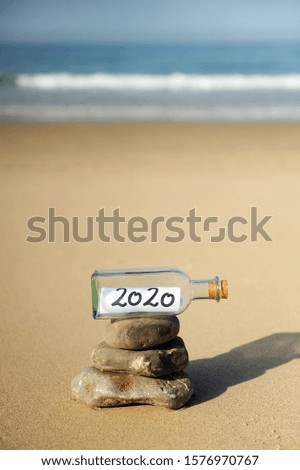 Happy New Year 2020 party. Message in a bottle found on the beach on stones in balance. Zen style summer vacation concept. 