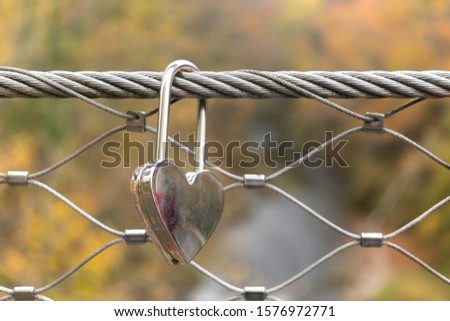 Love lock locked on the bridge. Silver colored padlock hanging on a wire rope