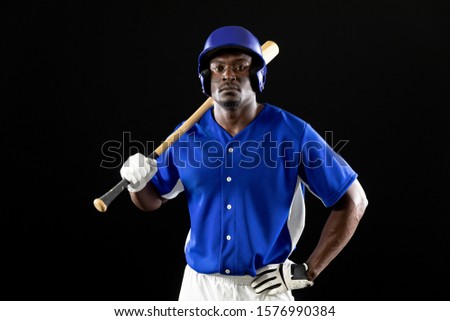 Portrait of an African American male baseball player, a hitter, wearing a team uniform and a helmet, holding a baseball bat on his shoulder, his hand on his hip 