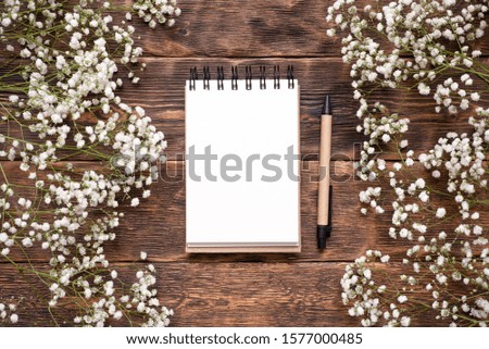Blank page notepad, pen and gypsophila flower plant on brown wooden table background.