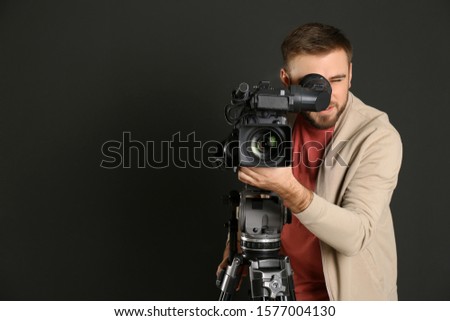 Operator with professional video camera on black background, space for text