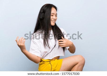 Teenager asian girl listening music over isolated blue wall