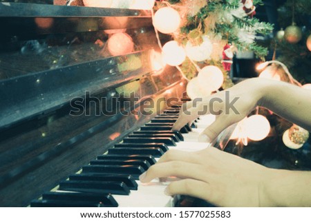 The hand is moving and playing the piano With a backdrop of lights and Christmas trees decorated by Christmas accessories that make the Christmas feel