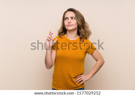 Young blonde girl over isolated background with fingers crossing and wishing the best