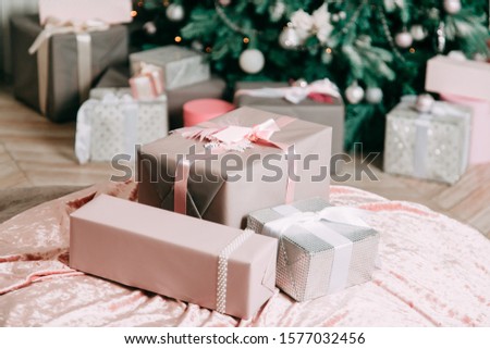 New Year's decor idea for a living room with gifts under a Christmas tree. Delicate pink and white balls and beads on fir tree branches, a pile of light gift boxes