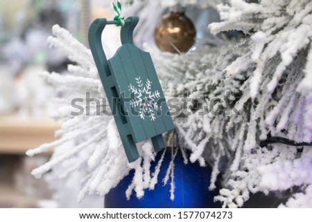 Christmas wooden toy sled on blue color on winter pine tree with white branch close up. Winter still life. Winter holiday composition.