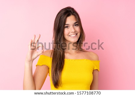 Teenager Brazilian girl over isolated pink background showing ok sign with fingers
